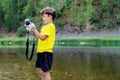 A schoolboy is standing in outdoor near the forest, holding a photo camera in his hands and washing, cleaning it with soap Royalty Free Stock Photo