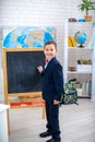 Schoolboy stands near blackboard in classroom and writes on the blackboard