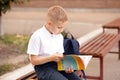 Schoolboy in uniform sitting on a bench and reading schoolbook