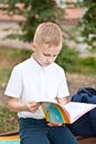 Schoolboy in uniform sitting on a bench and reading schoolbook