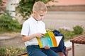 Schoolboy in uniform sitting on a bench and reading schoolbook