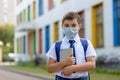 A schoolboy in a white shirt, blue tie and a backpack stands in a medical mask with a tablet Royalty Free Stock Photo