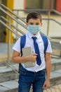 A schoolboy in a white shirt, blue tie and a backpack stands in a medical mask with a tablet Royalty Free Stock Photo