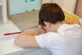 A schoolboy in a white T-shirt, tired of sitting at the monitor with a laptop, holding his head in his hands Royalty Free Stock Photo