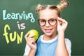 schoolchild holding apple and touching glasses near blackboard with learning is
