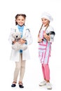 schoolchildren in costumes of doctor and chef standing with teddy bear and frying pan