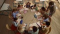 Schoolchildren having lesson at round table. Male teacher helping kids at lesson Royalty Free Stock Photo