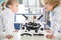 Schoolchildren in lab coats using microscopes and looking at each other