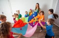Schoolchildren playing using parachute with friends in gym