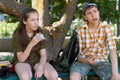 schoolchildren, a teenage boy and a girl are sitting on a bench in a city park and eating sandwiches, a bright summer day Royalty Free Stock Photo