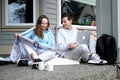 schoolchildren teenagers on doorstep at home doing homework boy in hands of laptop girl has big white folder two cups of Royalty Free Stock Photo