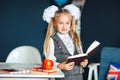 Schoolgirl blondy in school uniform with white bows standing near the table and studying in the classroom. Education and school