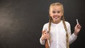 Schoolgirl with book and piece of chalk smiling at camera against blackboard