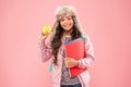 Schoolgirl with books after lesson. school break. small happy girl earflap hat eat apple. winter holiday vacation. teen