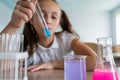 A schoolgirl conducts experiments in a chemistry lesson. Girl pouring colored liquids from a beaker.