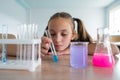 A schoolgirl conducts experiments in a chemistry lesson. Girl pouring colored liquids from a beaker.