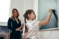 Schoolgirl first-grader writing on chalkboard. School lesson Teacher and pupil. Royalty Free Stock Photo