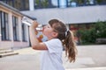 Schoolgirl girl drinks fresh mineral water from a bottle in the schoolyard. Take a break from school. Quenching thirst, Royalty Free Stock Photo