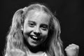 Schoolgirl has paint spots on face holds fists up. Girl with happy face stands on black background, close up.