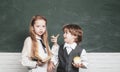 Schoolgirl helping pupils studying at desks in classroom. Teacher and child. Blackboard background. Little children at Royalty Free Stock Photo