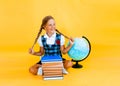 Schoolgirl isolated on yellow background with globe. little girl in school uniform sitting on a yellow background, reading a book Royalty Free Stock Photo