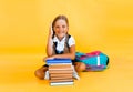 Schoolgirl isolated on yellow background with globe. little girl in school uniform sitting on a yellow background, reading a book Royalty Free Stock Photo