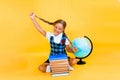 Schoolgirl isolated on yellow background with globe. little girl in school uniform sitting on a yellow background, reading a book Royalty Free Stock Photo