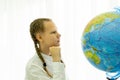 A schoolgirl with pigtails and a white shirt sitting at her desk is looking at a globe in a school classroom. The