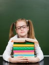 Schoolgirl with pile books near empty green chalkboard