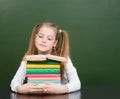 Schoolgirl with pile books near empty green chalkboard