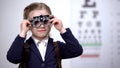 Schoolgirl putting optical trial frame to determine visual acuity, optometrist