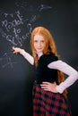 A schoolgirl with red long hair in a school uniform stands near school board Royalty Free Stock Photo