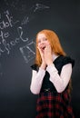 A schoolgirl with red long hair in a school uniform stands near school board Royalty Free Stock Photo