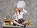 The schoolgirl in school uniform sits on table and thinks with comic balloon. Child education concept.