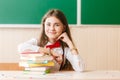 Schoolgirl in school uniform sitting at her desk with books and pencils on the background of a green board Royalty Free Stock Photo
