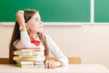 Schoolgirl in school uniform sitting at her desk with books and pencils on the background of a green board Royalty Free Stock Photo