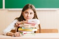 Schoolgirl in school uniform sitting at her desk with books and pencils on the background of a green board Royalty Free Stock Photo