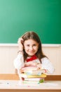 Schoolgirl in school uniform sitting at her desk with books and pencils on the background of a green board Royalty Free Stock Photo