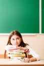 Schoolgirl in school uniform sitting at her desk with books and pencils on the background of a green board Royalty Free Stock Photo