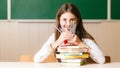 Schoolgirl in school uniform sitting at her desk with books and pencils on the background of a green board Royalty Free Stock Photo