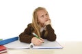 Schoolgirl in school uniform sitting at studying desk doing homework looking thoughtful and absent mind Royalty Free Stock Photo