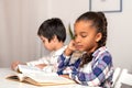 The schoolgirl and schoolboy siting at the table indoors and doing their homework