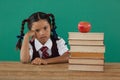 Schoolgirl sitting beside books stack with apple on top against chalkboard Royalty Free Stock Photo