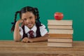 Schoolgirl sitting beside books stack with apple on top against chalkboard Royalty Free Stock Photo