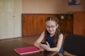 Schoolgirl sitting at the table with textbooks in the classroom. Girl in a blue dress with pigtails