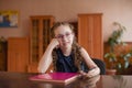 Schoolgirl sitting at the table with textbooks in the classroom. Girl in a blue dress with pigtails