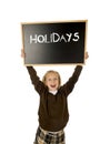 Schoolgirl smiling happy holding and showing blackboard with text holidays in end of school Royalty Free Stock Photo