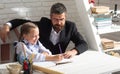 Schoolgirl studying and writing in classroom with teacher. Cute pupil girl studies with happy face expression near desk