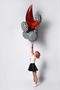 Schoolgirl in t-shirt, red headband, black skirt and sneakers. Holding balloons, posing sideways isolated on white. Full length Royalty Free Stock Photo