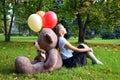 Sad baby girl with big teddy bear and balloons in the park. Problems teenagers at school